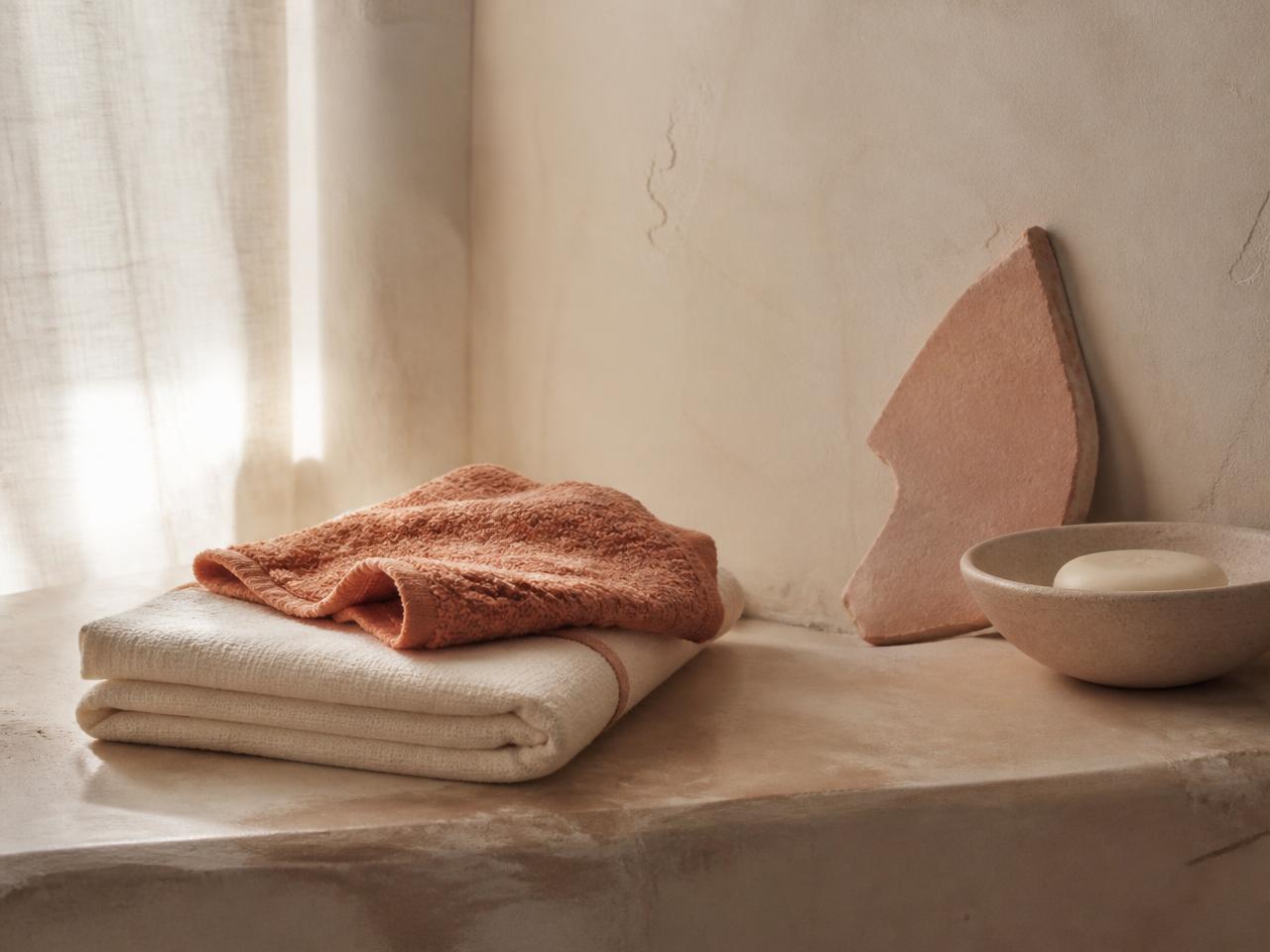 Folded cream cotton underwear and a dried flower stem on a warm plaster ledge