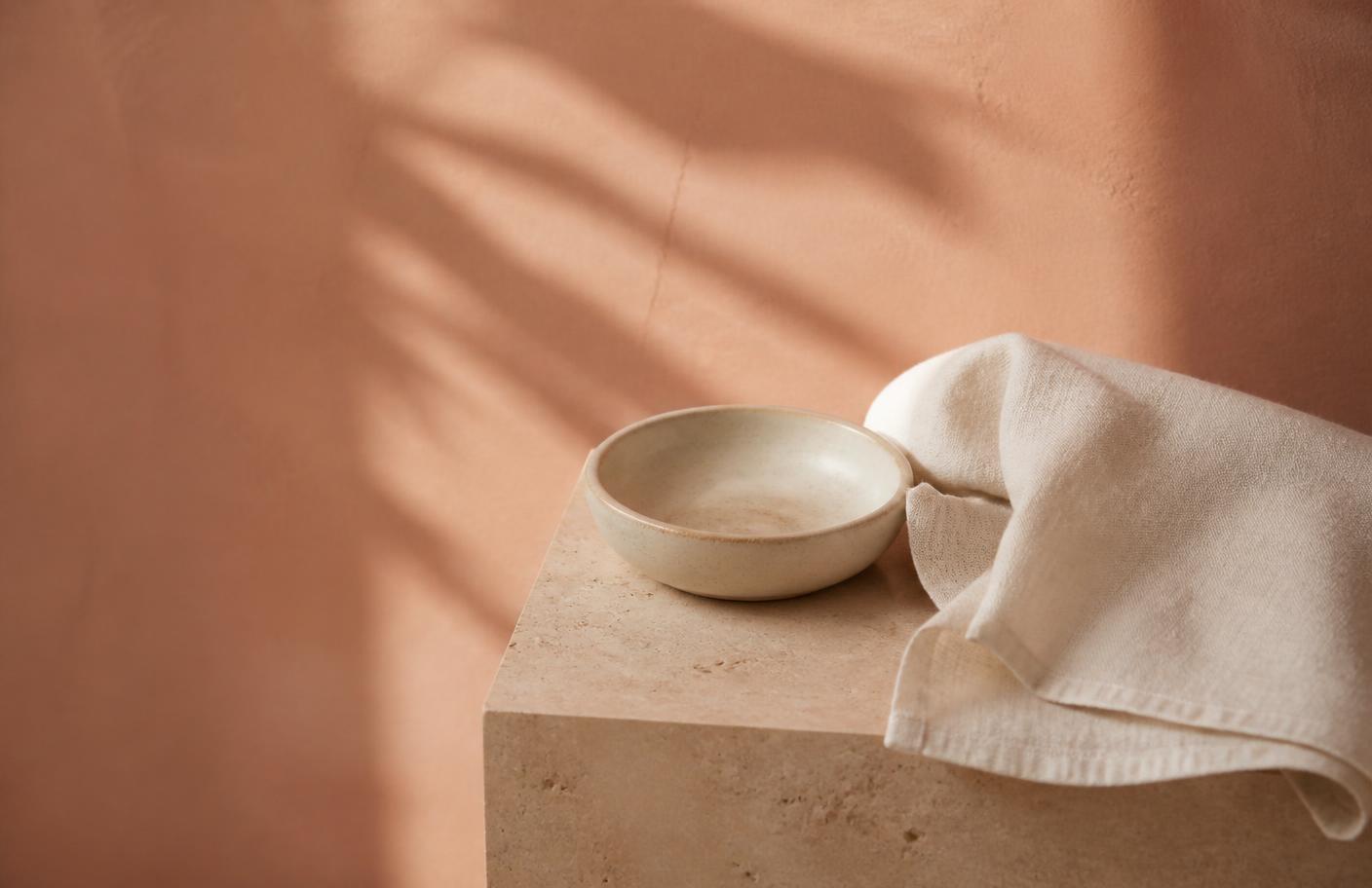 Coral freya. Vee razor resting on a folded cream linen towel on a warm clay bathroom ledge