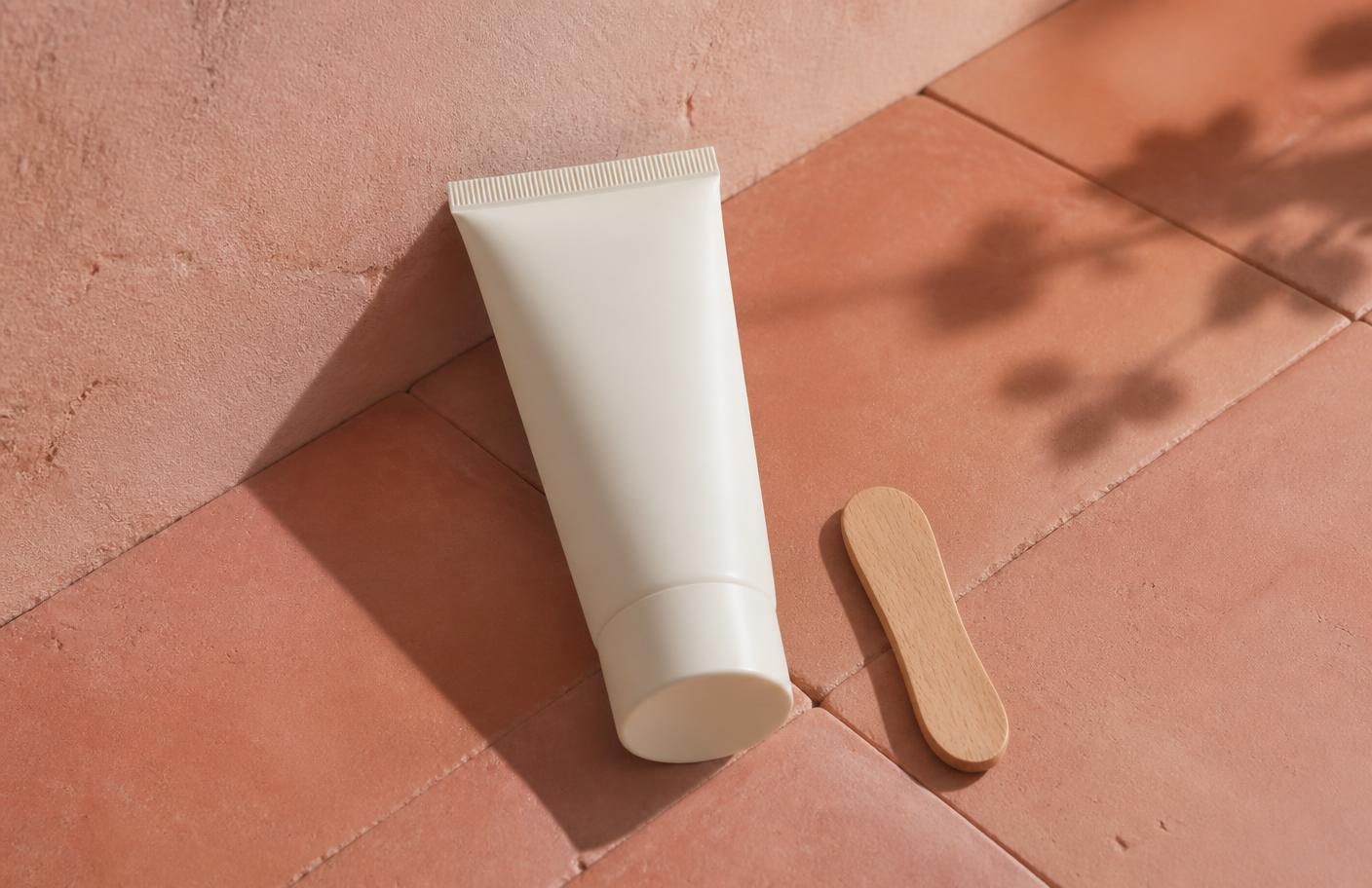 An open tube of hair removal cream with a spatula applicator, blush waffle towels and a timer